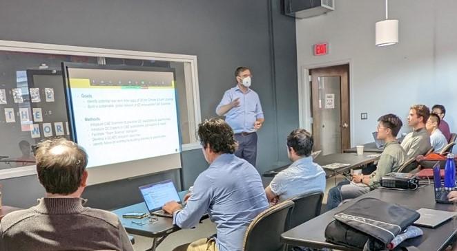 man speaking at a workshop in front of projector screen